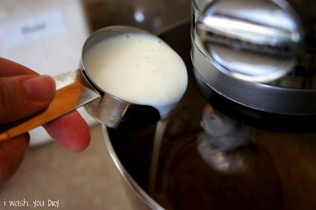 A hand pouring a measuring cup of buttermilk into a mixing bowl