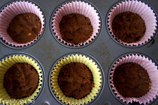 A muffin pan with filled with cupcake wrappers with at the bottom of each covered with a flattened crust.
