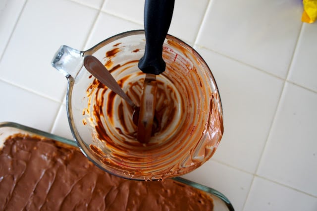 A close up of glass measuring cup with remnants of melted chocolate next to a pan of chocolate covered Rice Krispie Treats