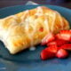 A close up of a Homemade Strawberry and Cream Cheese Toaster Strudel on a plate, with a side of diced strawberries