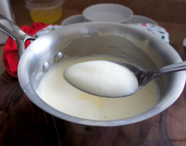 A pot with a egg/creme mixture with a spoon above it filled with a think layer of foam