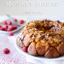 A breaded desert on a plate on a table, topped with almond slices, gooey sauce and raspberries