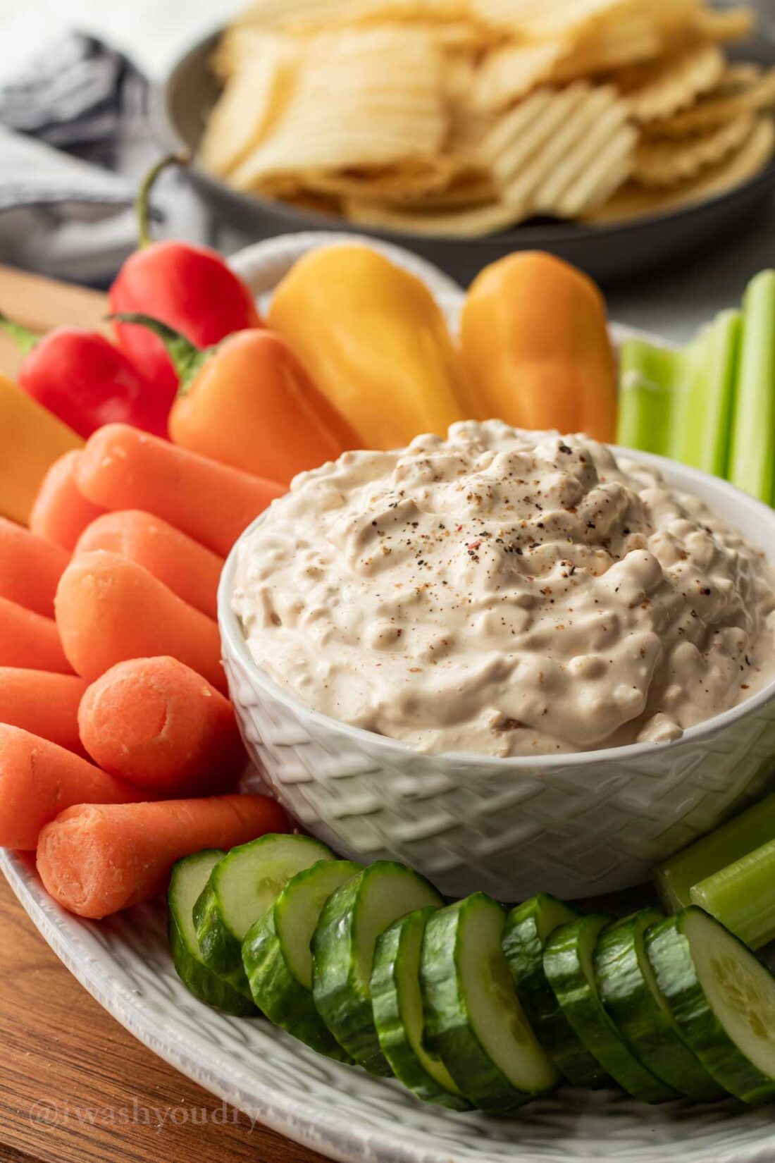 chip dip in white bowl with veggies around it.
