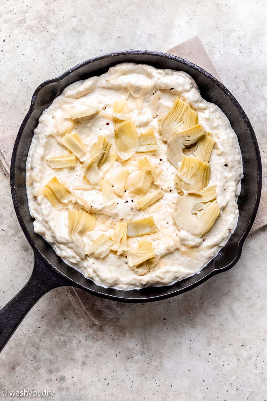 Unbaked artichoke dip in black pan on marble countertop.