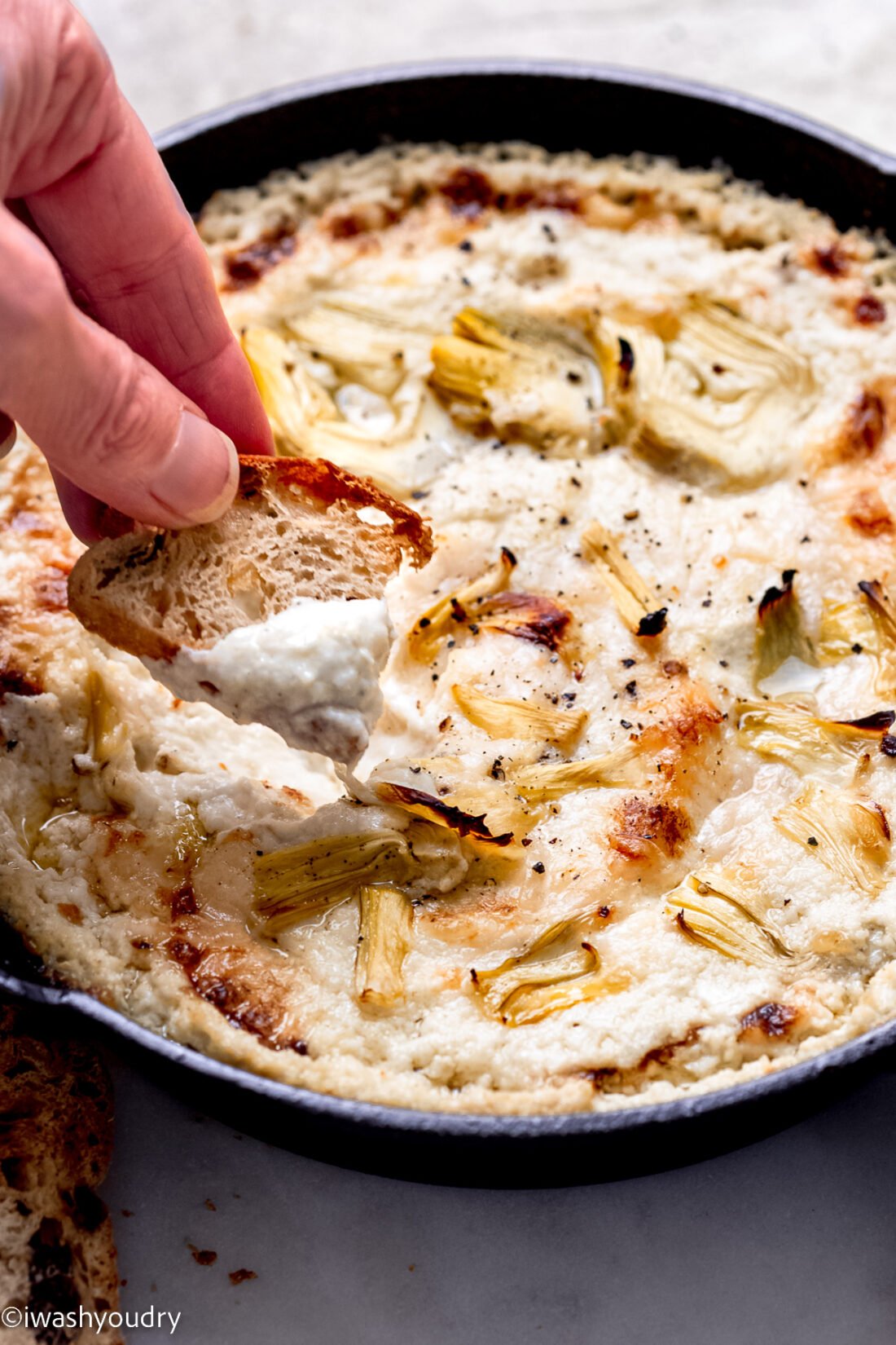Hand scooping baked dip onto bread. 