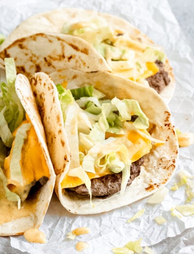 three small tacos with beef and cheese topped with lettuce and big mac sauce.