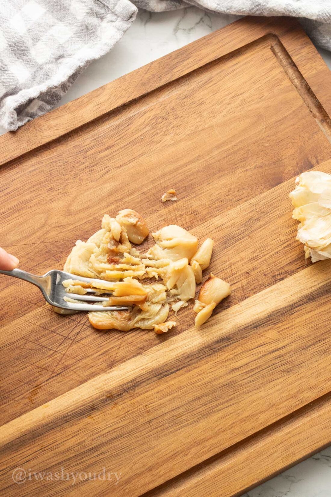 Fork mashing roasted garlic on wood cutting board.