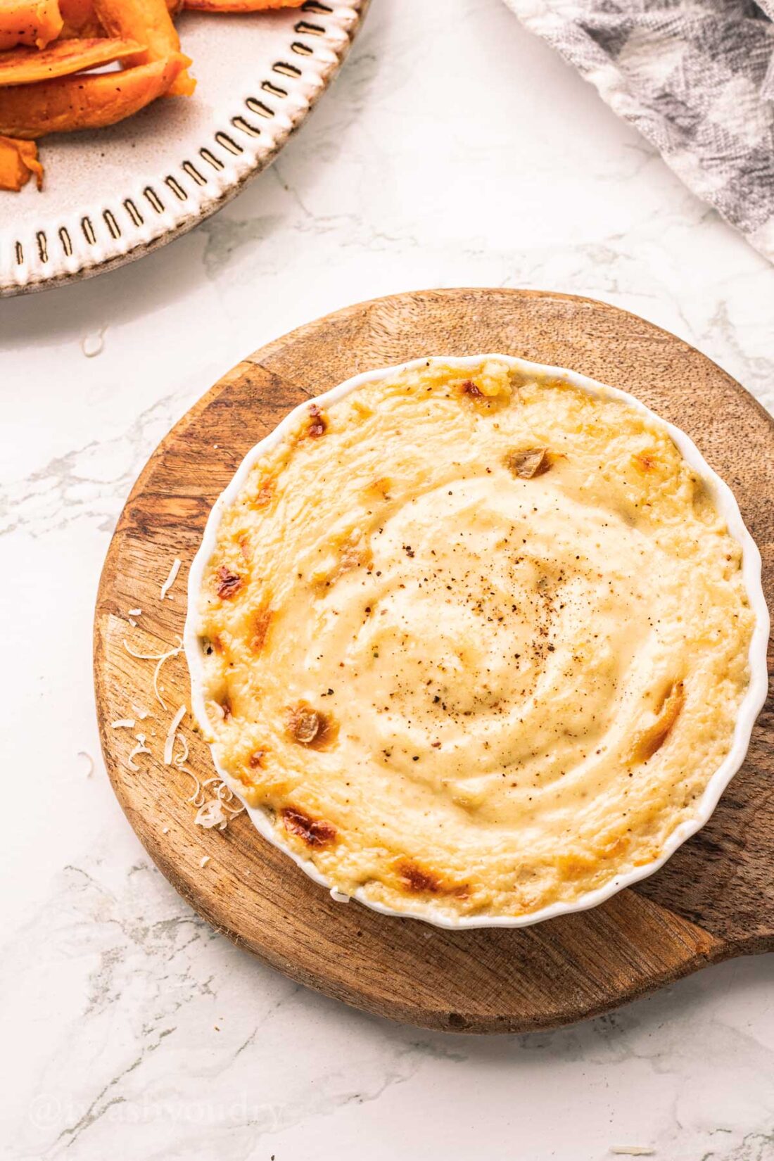 Overhead view of baked creamy roasted garlic dip on wood platter.