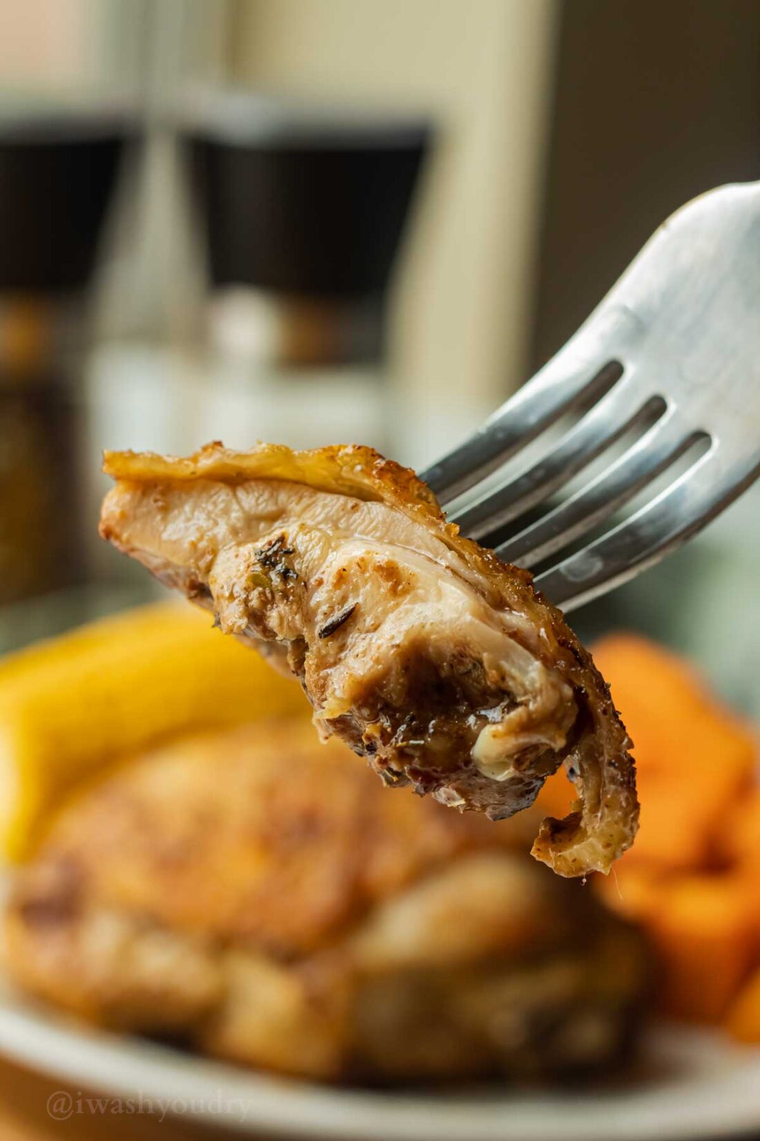 Bite of juicy chicken on a fork above plate of food.