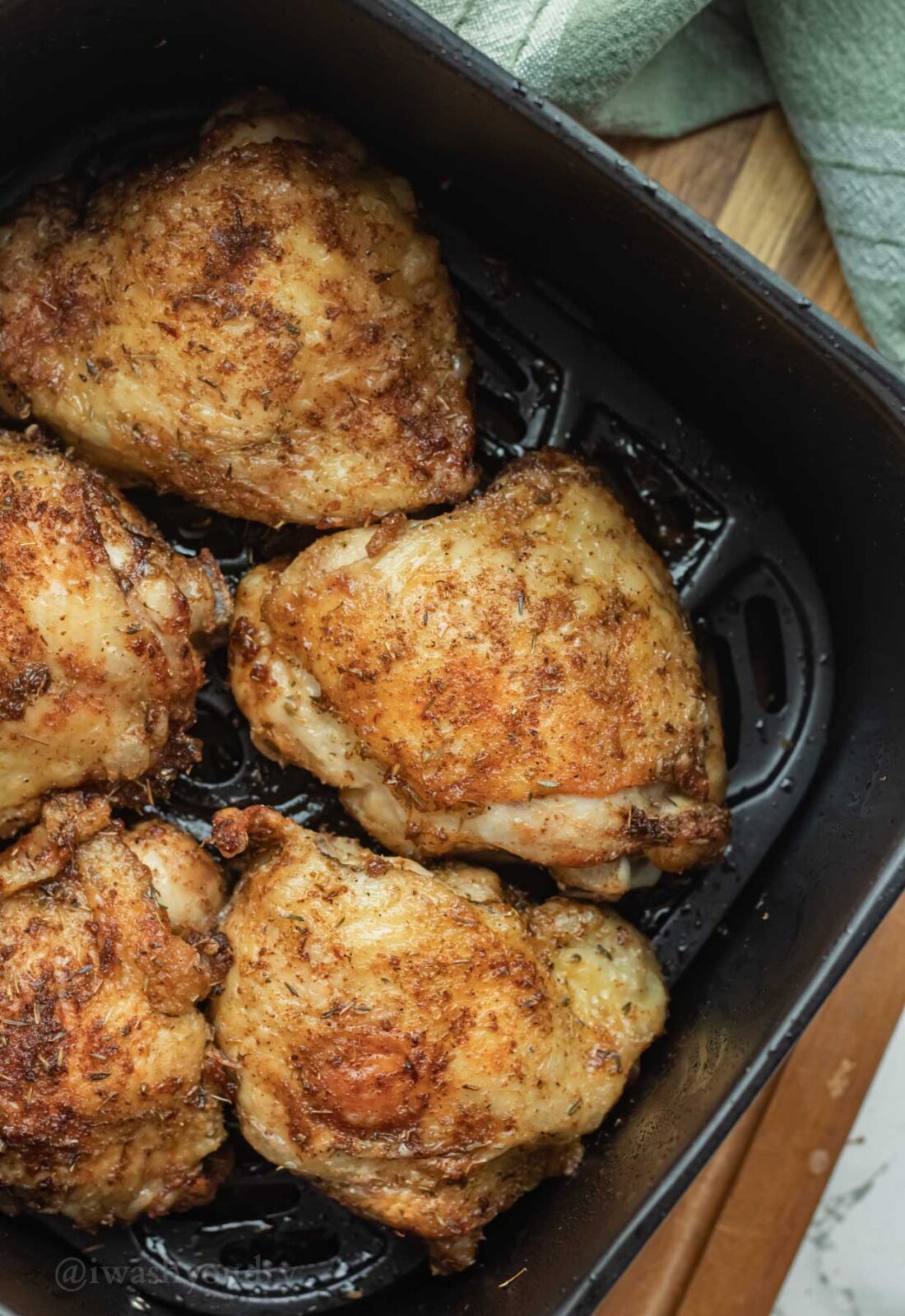 Cooked chicken thighs with crispy skin in basket of air fryer.