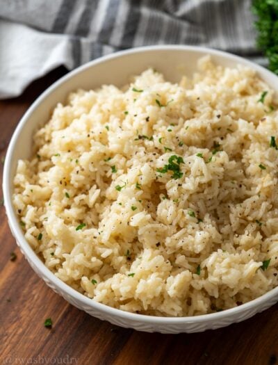 Cooked white rice pilaf in textured white bowl with chopped parsley on top.