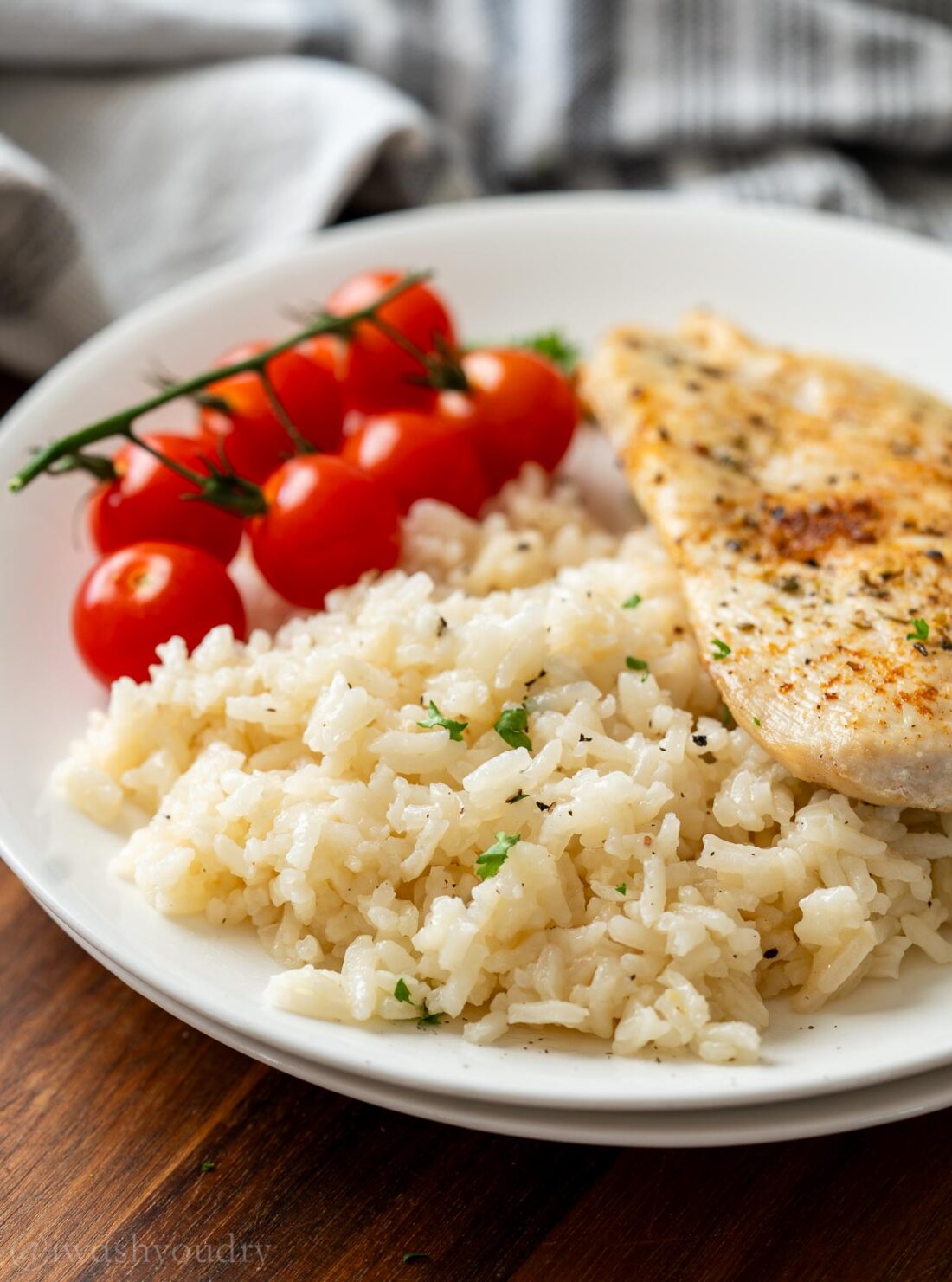Butter rice pilaf on white plate with vine tomatoes and cooked chicken.
