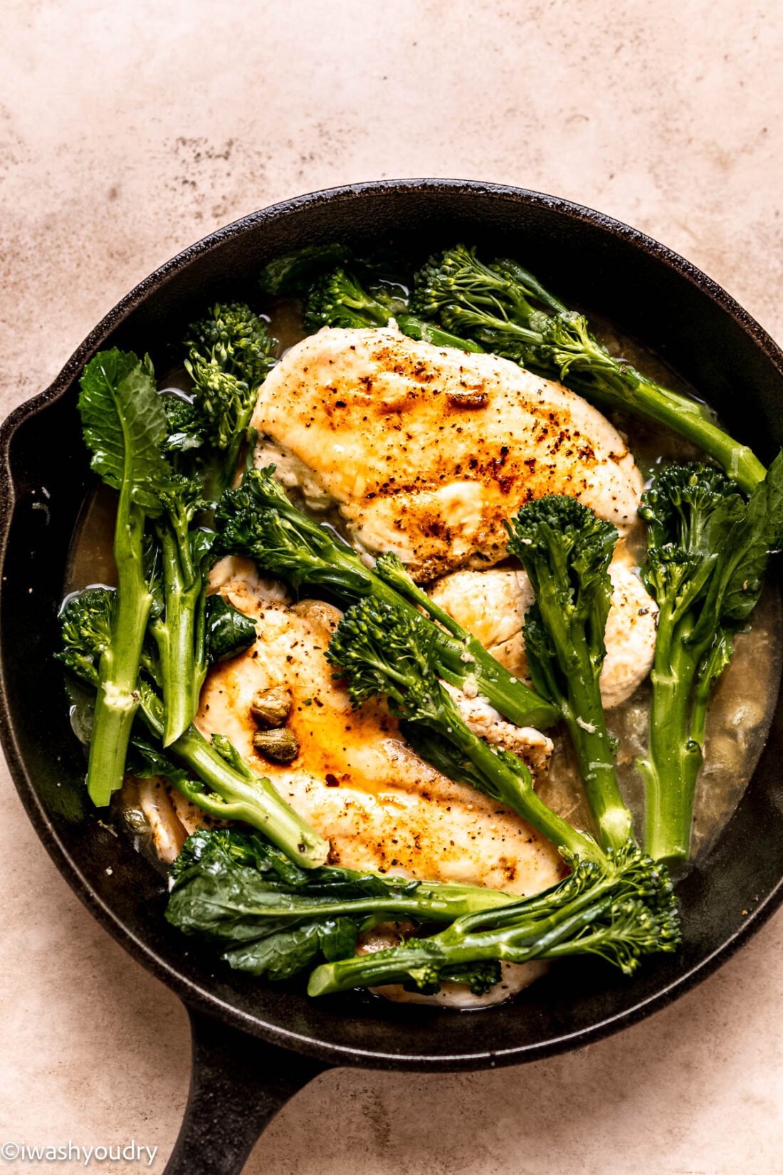 Cooking chicken and broccolini in frying pan.
